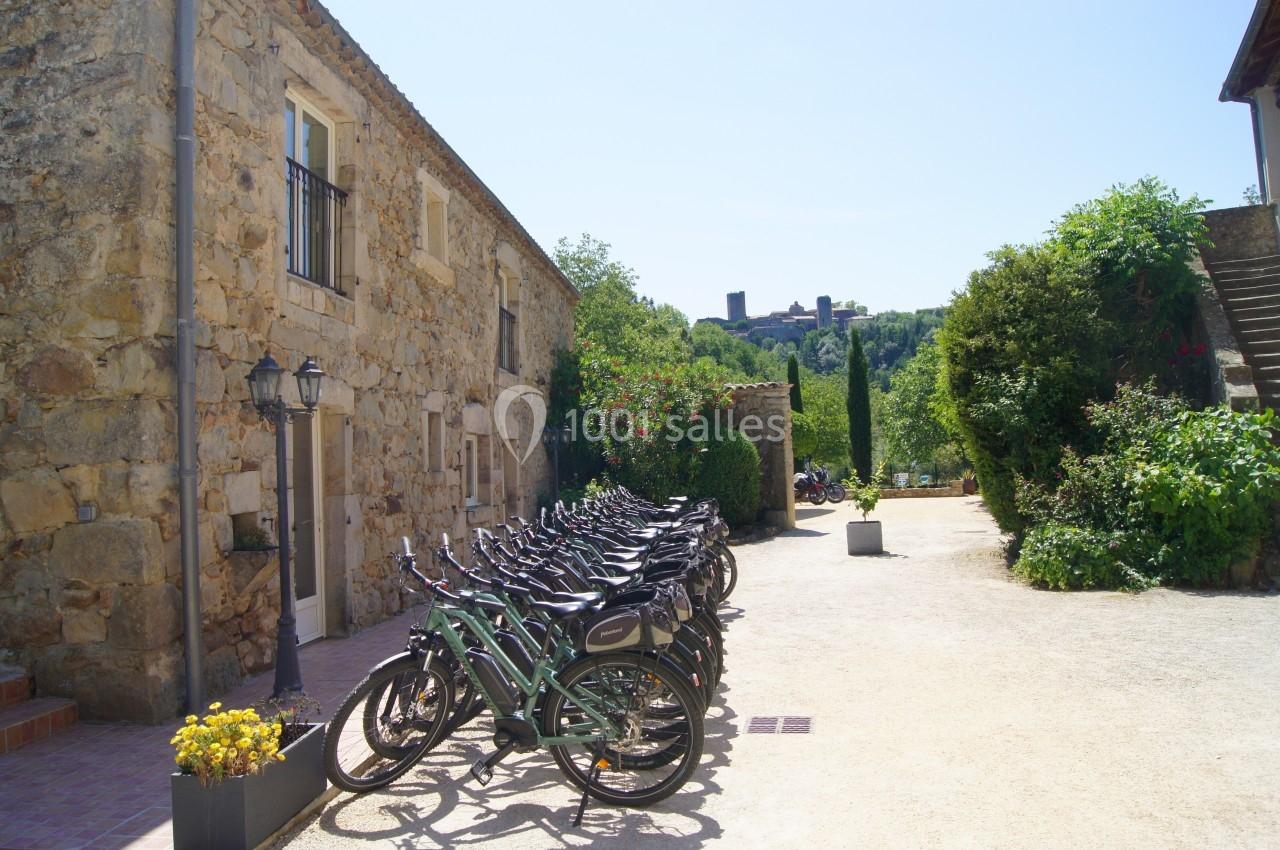 Rangée de vélos alignés devant un bâtiment en pierre, avec un paysage de village et une tour en arrière-plan.