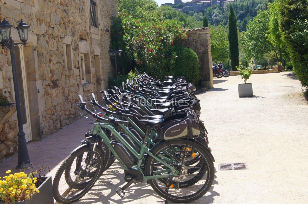 Rangée de vélos électriques stationnés devant un bâtiment en pierre, entouré de végétation.