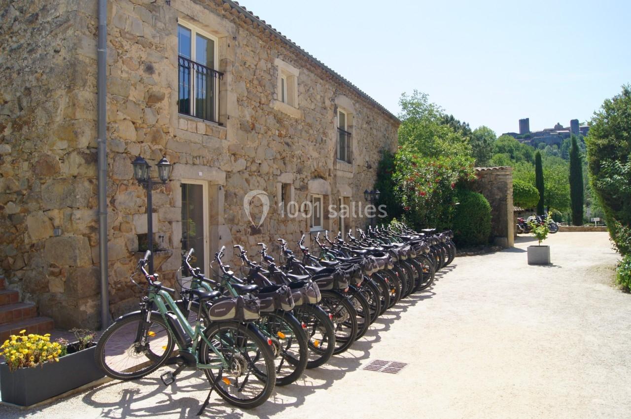 Alignement de vélos électriques devant un bâtiment en pierre, entouré de végétation et baigné de lumière naturelle.