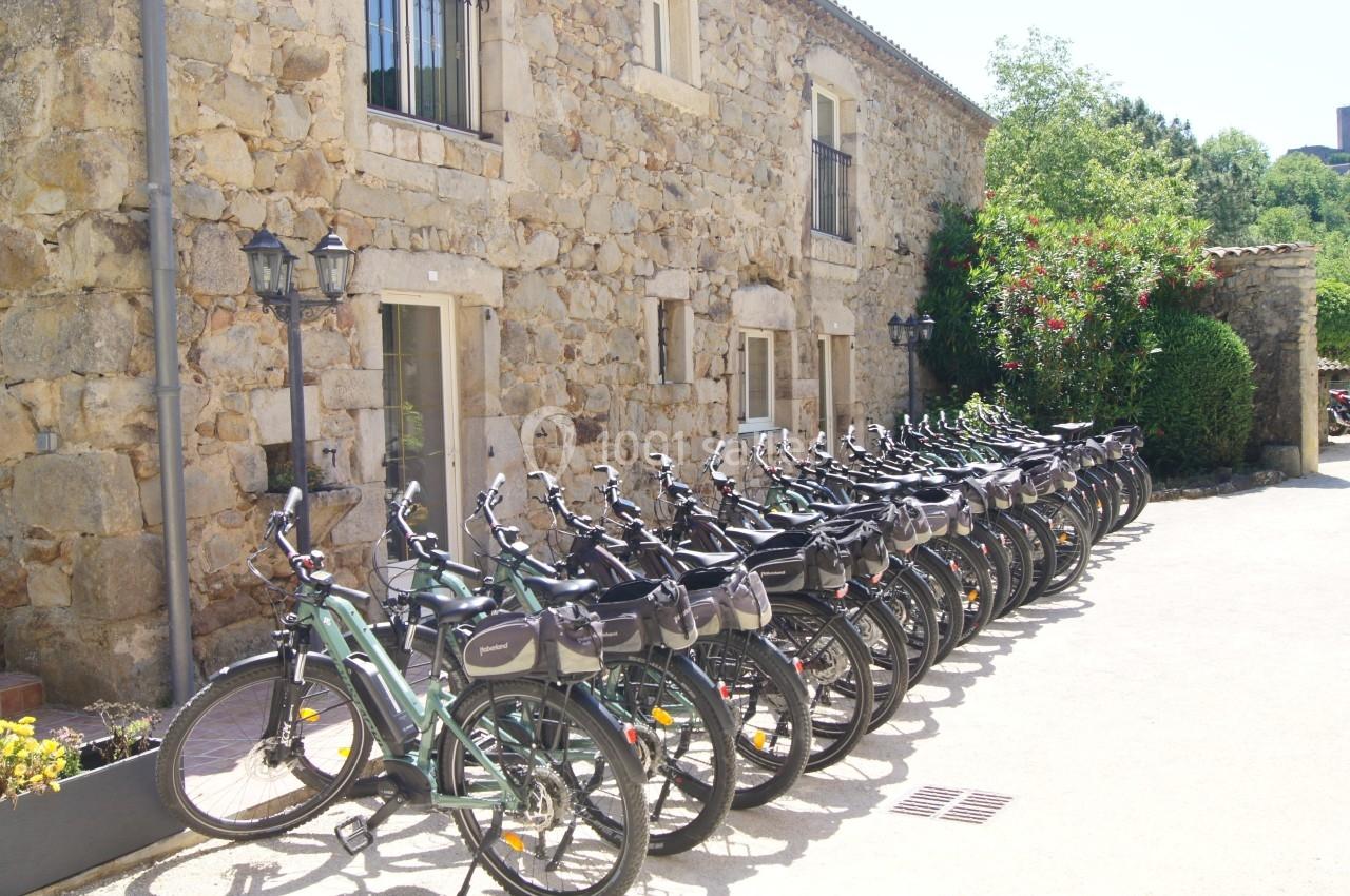 Alignement de vélos électriques stationnés devant un bâtiment en pierre sous un ciel ensoleillé.