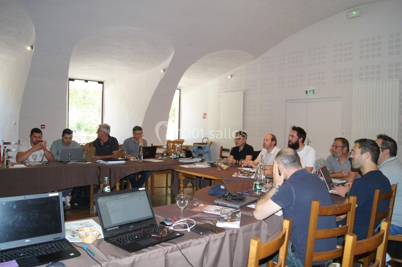Un groupe de personnes assises autour de tables en réunion dans une salle lumineuse avec des ordinateurs portables.