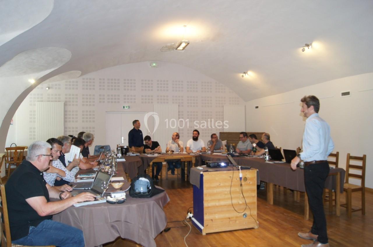 Un groupe de personnes assises autour de tables en réunion dans une salle avec un plafond voûté.