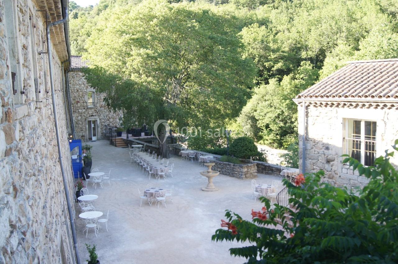 Cour extérieure avec tables et chaises disposées près de bâtiments en pierre, entourée de végétation dense.