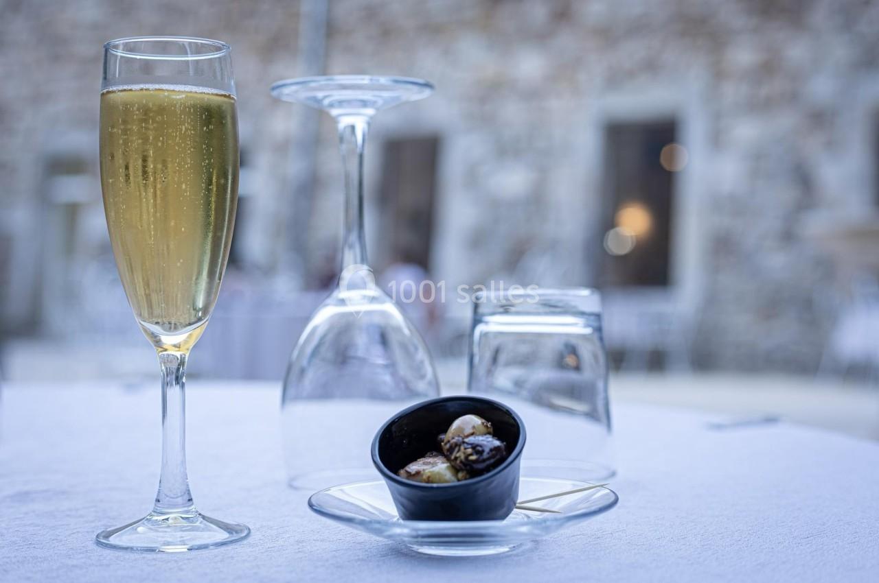 Verre de champagne, verrines et verrerie renversée sur une table blanche en extérieur avec un mur en pierre en arrière-plan.