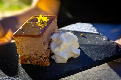 Part de gâteau au caramel décorée d'une fleur jaune, accompagnée de chantilly, servie sur une ardoise noire.