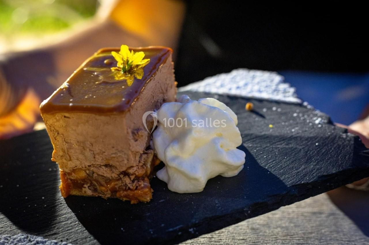 Part de gâteau au caramel décorée d'une fleur jaune, accompagnée de chantilly, servie sur une ardoise noire.
