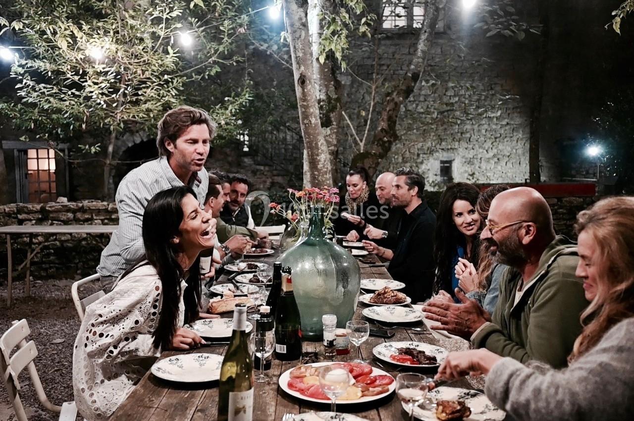 Un groupe de personnes partage un repas convivial en soirée dans un jardin éclairé par des guirlandes lumineuses.