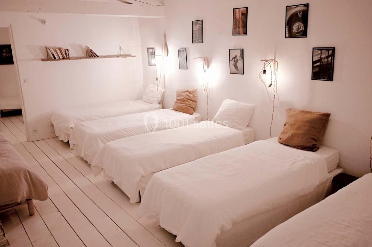 Chambre lumineuse avec cinq lits simples alignés, décorée de cadres et d'étagères minimalistes.