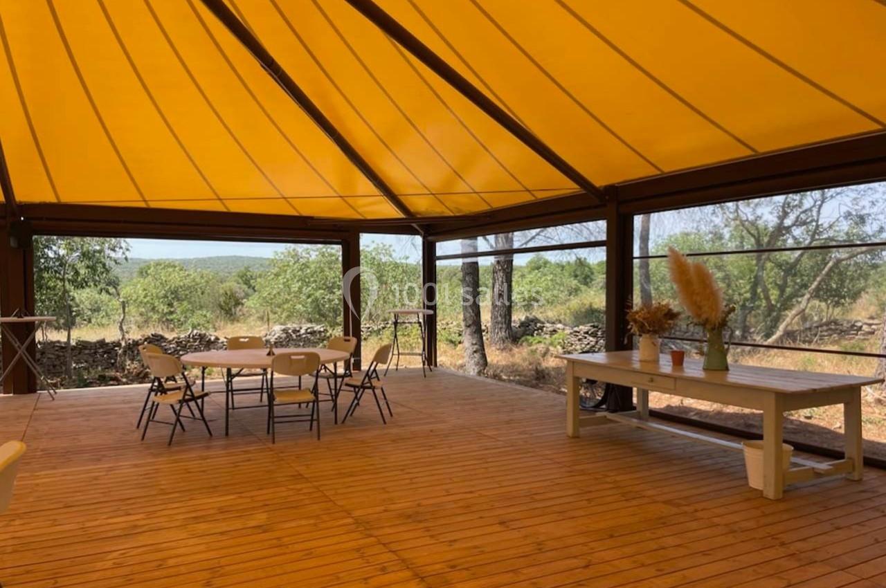 Terrasse en bois couverte d'une toile jaune, aménagée avec des tables, des chaises et une table décorée de plantes.