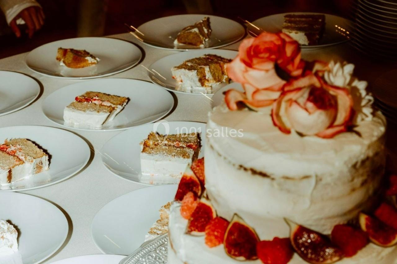Gâteau à étages décoré de fleurs et de fruits rouges, entouré d'assiettes contenant des parts de gâteau.