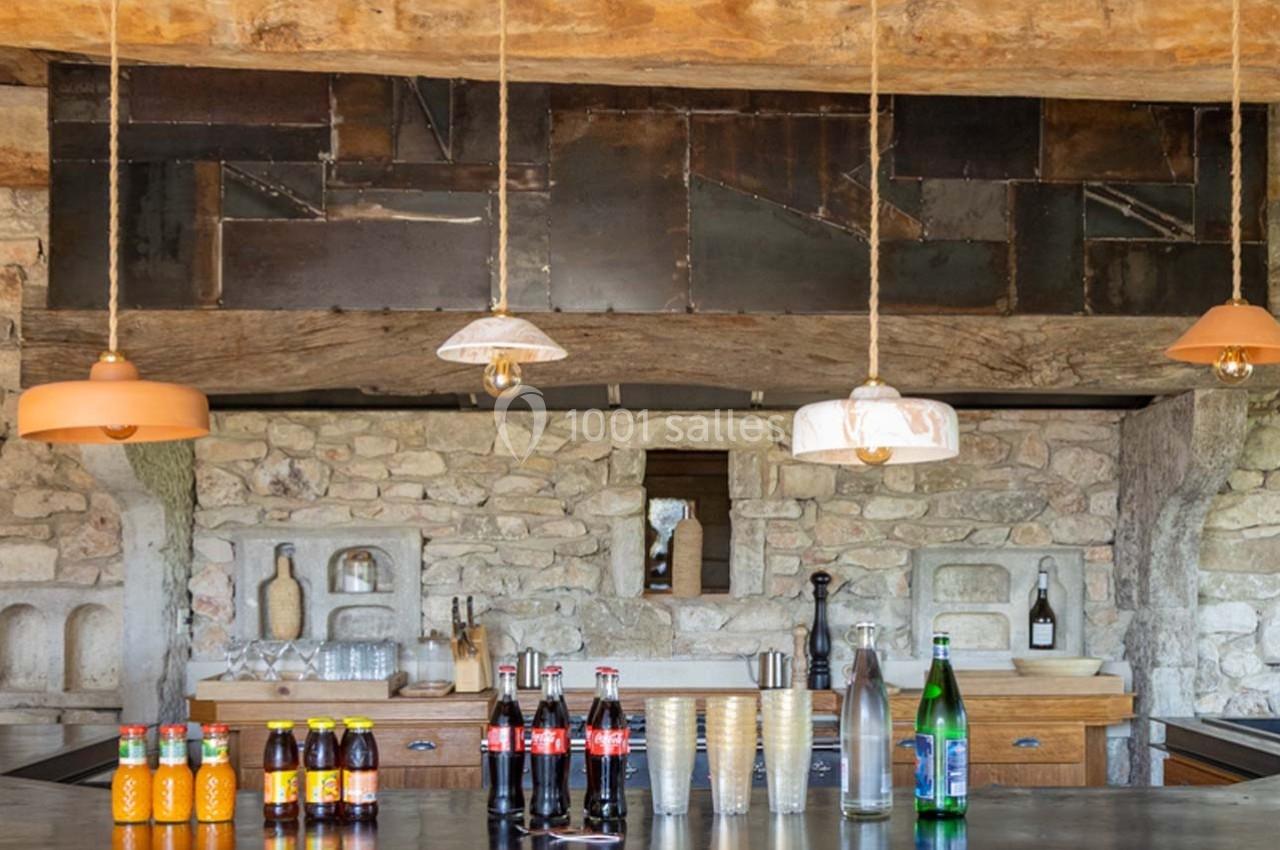 Comptoir de cuisine rustique avec boissons variées, suspensions lumineuses et mur en pierre apparente.