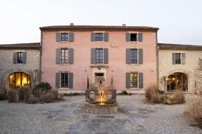Arbuste dense à feuillage vert brillant à côté d'un arbre taillé, dans un jardin ensoleillé avec pelouse et végétation.