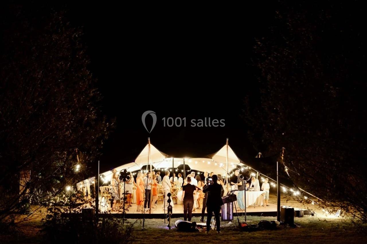 Tente éclairée la nuit accueillant un groupe de personnes lors d'un événement en plein air.