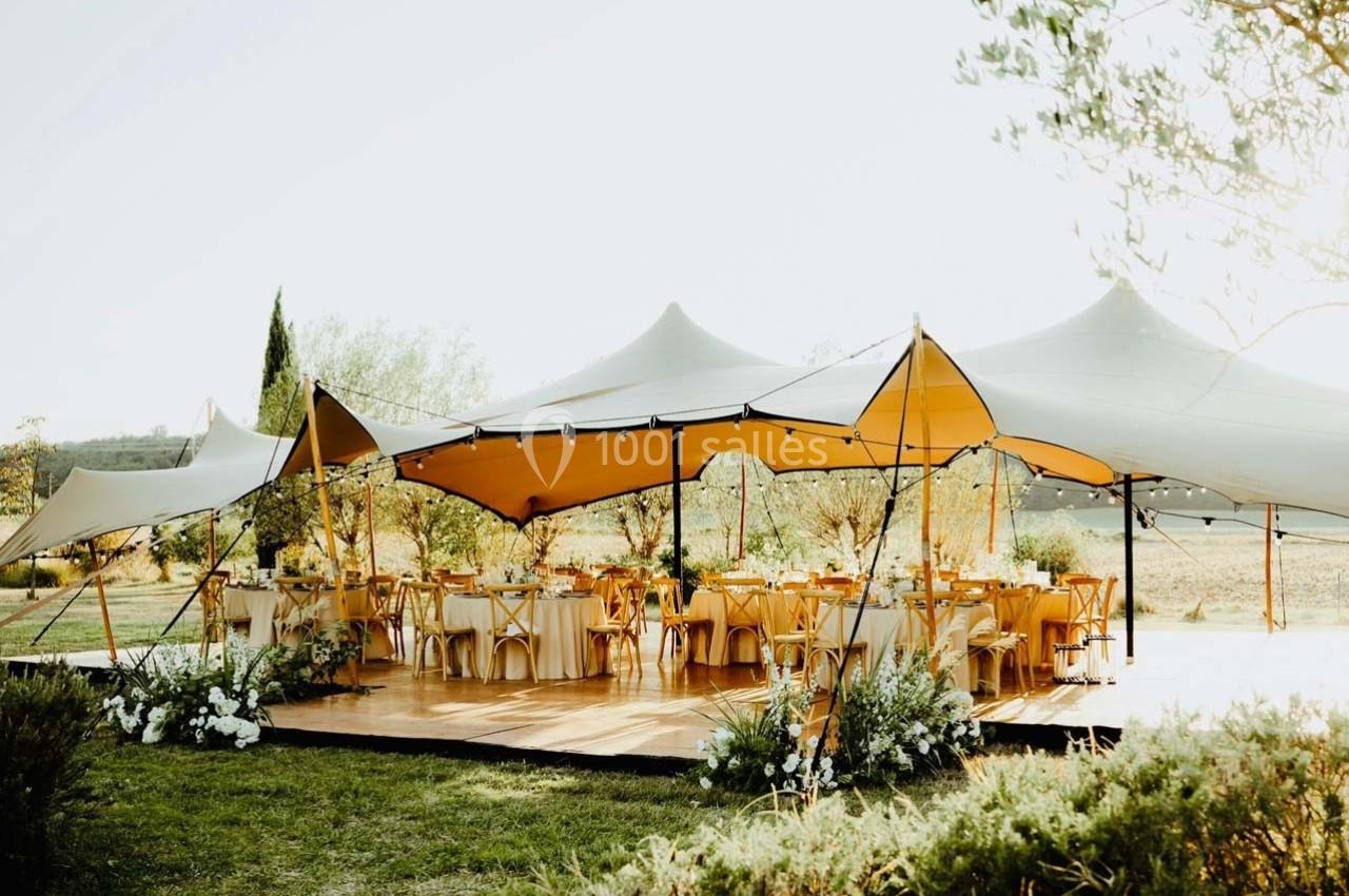 Tente beige installée en extérieur, abritant des tables décorées pour un événement dans un cadre naturel.