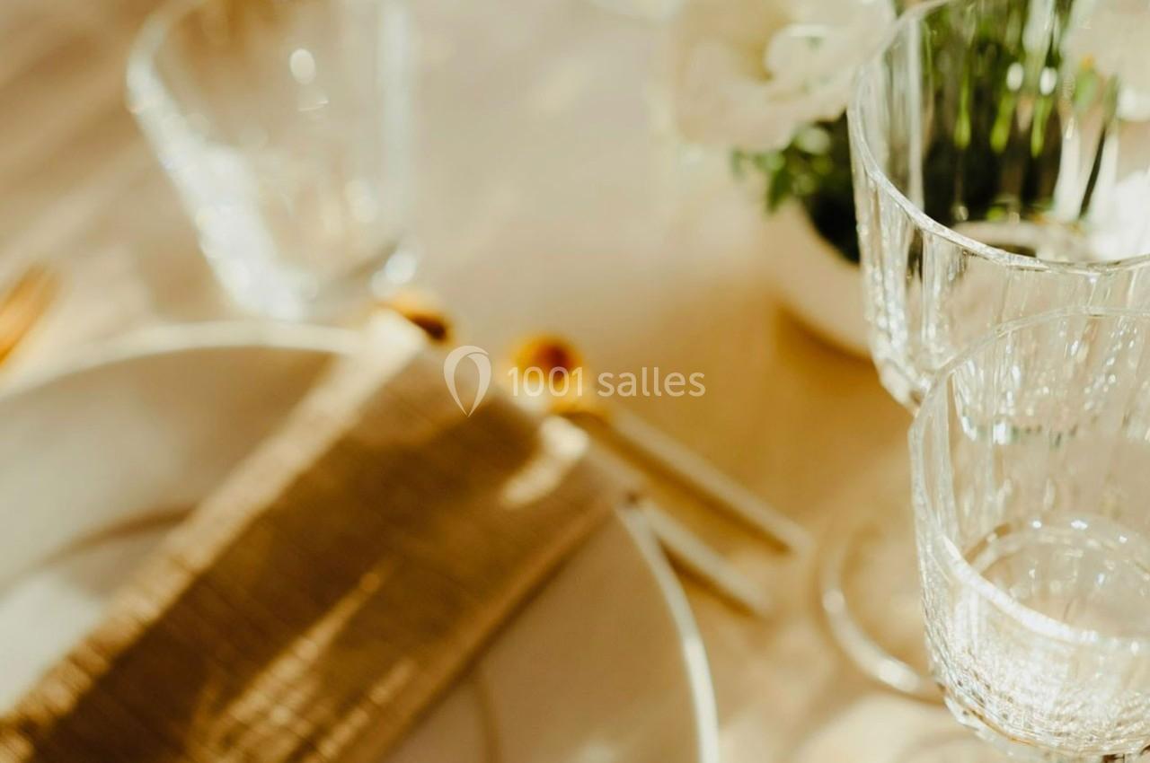 Table dressée avec des verres en cristal, une assiette blanche, une serviette beige et un bouquet de fleurs blanches en…