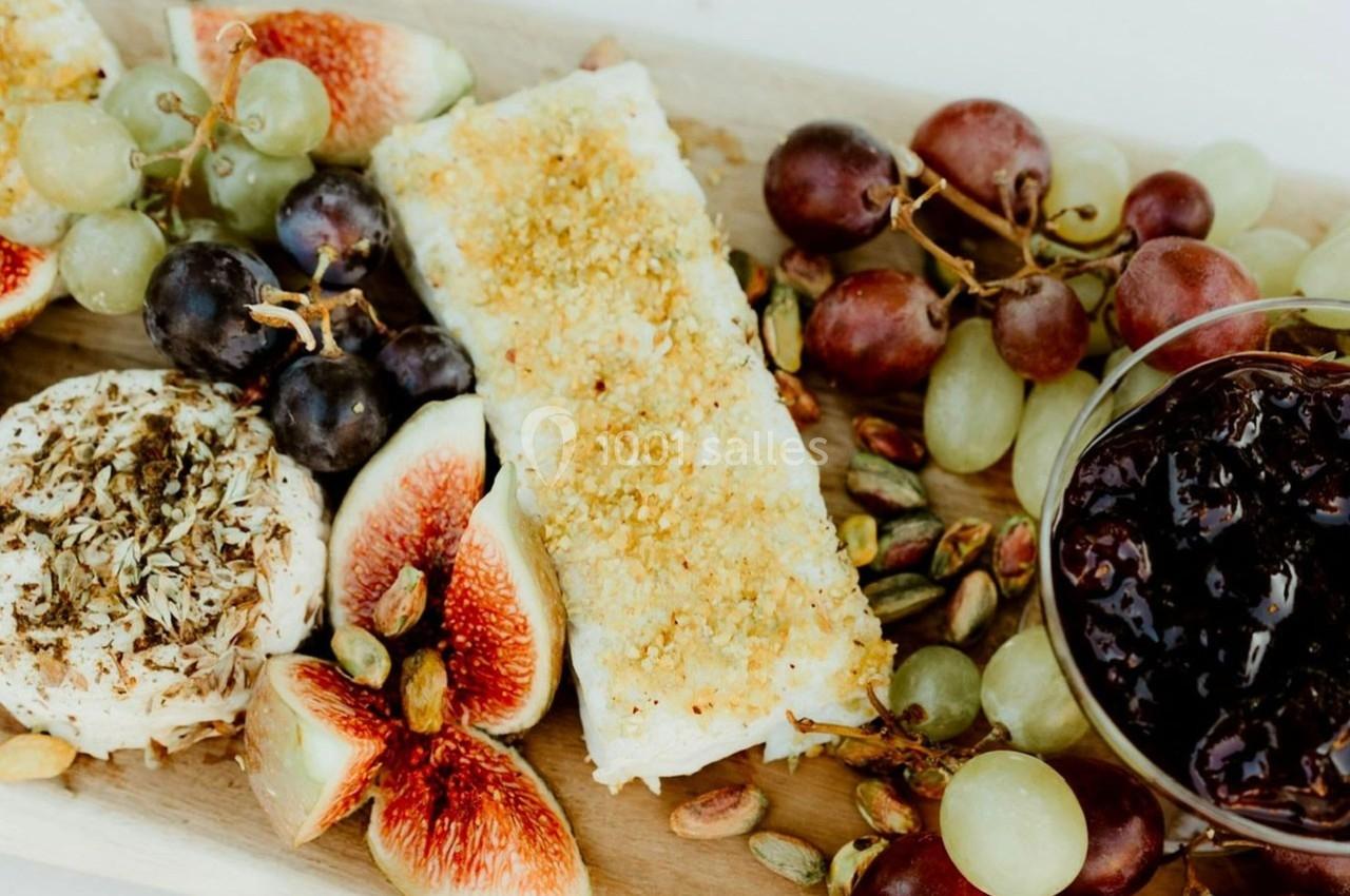 Plateau en bois avec fromage, figues fraîches, raisins, pistaches et confiture dans un bol en verre.