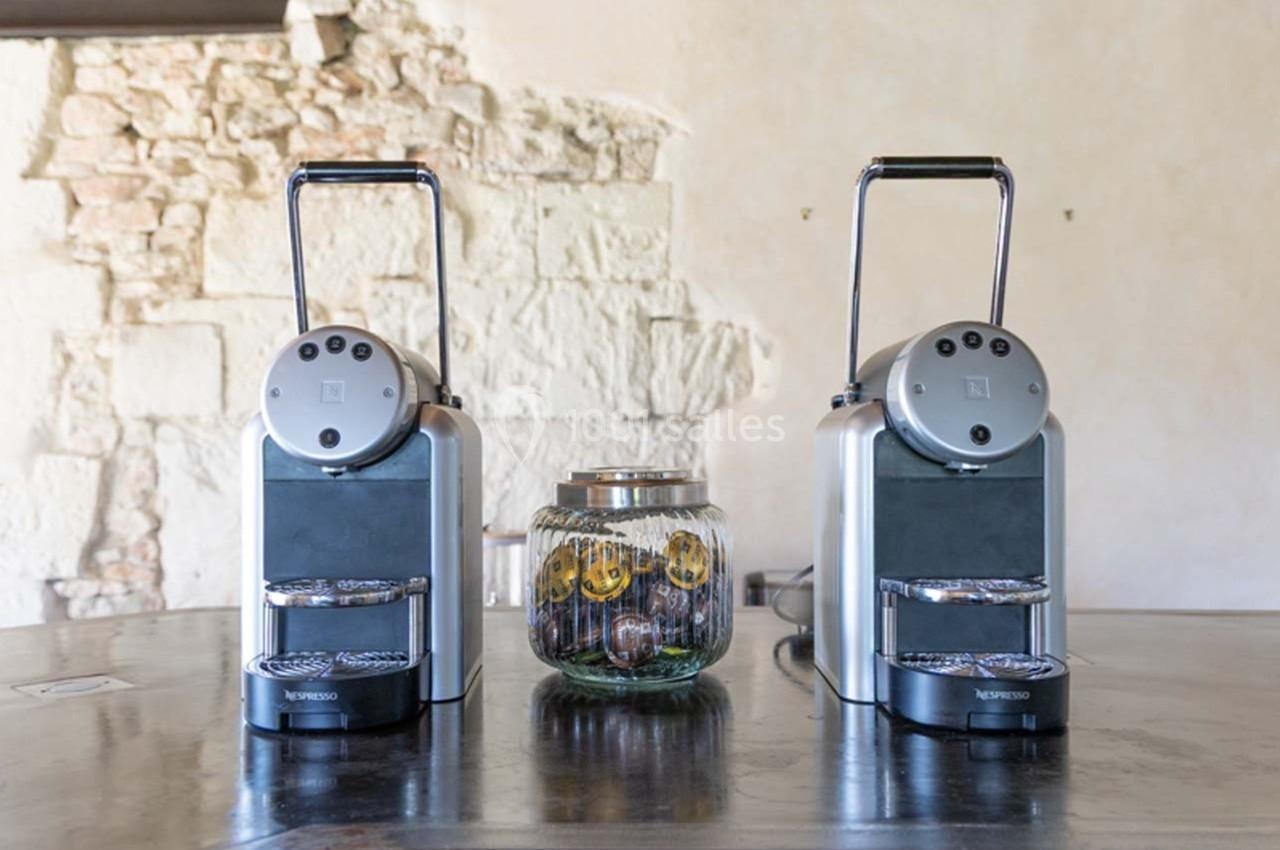 Deux machines à café argentées posées sur un comptoir en métal, avec un bocal de tranches de citron entre elles.