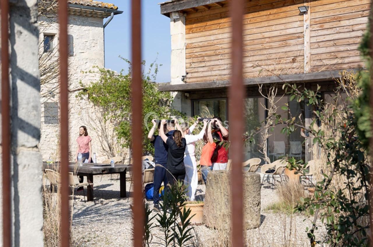 Un groupe de personnes participe à une activité en plein air dans une cour entourée de bâtiments en pierre et en bois.
