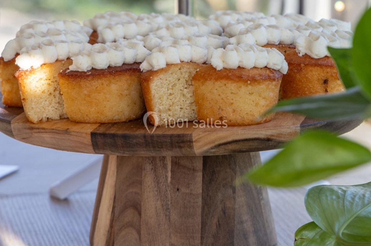 Des petits gâteaux moelleux avec glaçage blanc sont disposés sur un présentoir en bois, éclairés par la lumière naturelle.