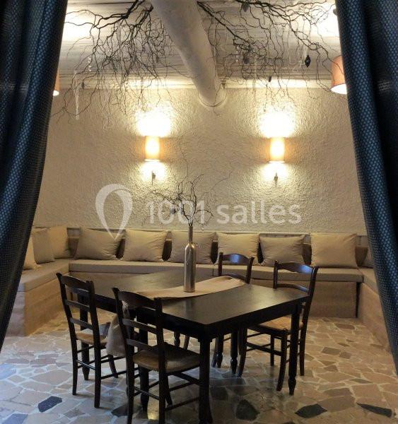 Salle avec des murs clairs, table en bois entourée de chaises, banquette beige et décoration de branches suspendues.