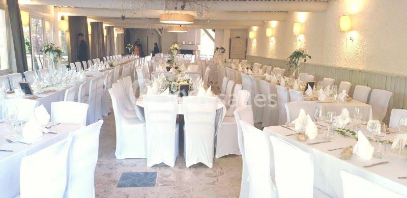 Salle de réception lumineuse avec tables dressées, nappes blanches et décorations florales.