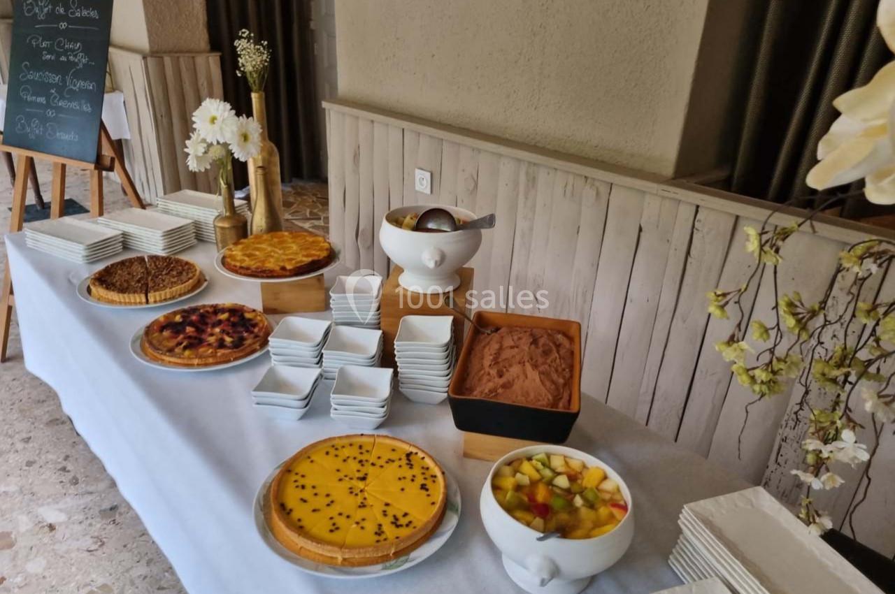 Buffet de desserts avec tartes, mousse au chocolat, salade de fruits et piles d'assiettes blanches.