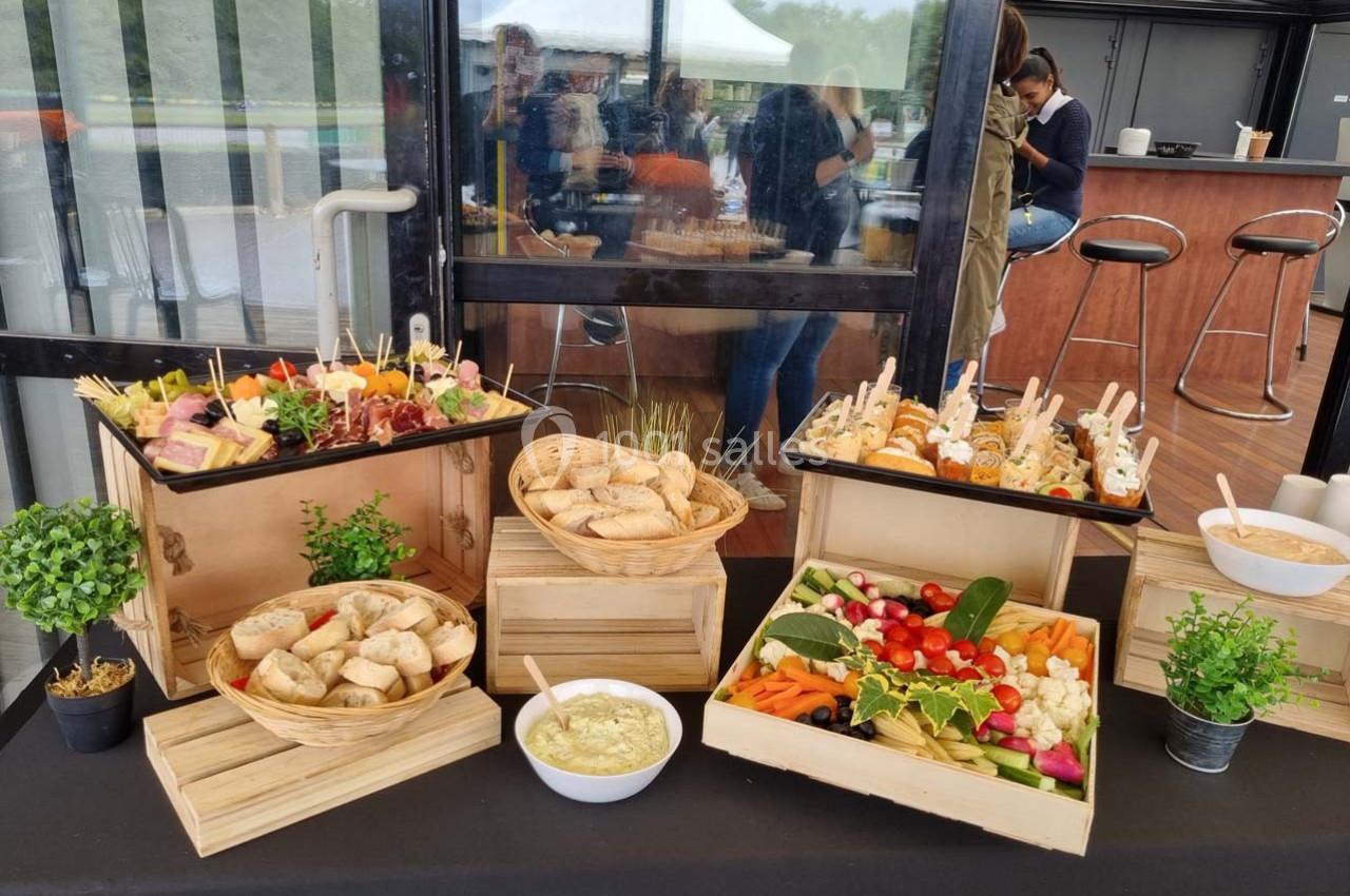 Buffet composé de pains, légumes frais, brochettes apéritives et sauces, disposé sur une table en extérieur couvert.