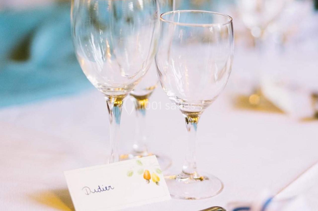Trois verres à pied vides posés sur une table blanche avec une carte de place portant un prénom.