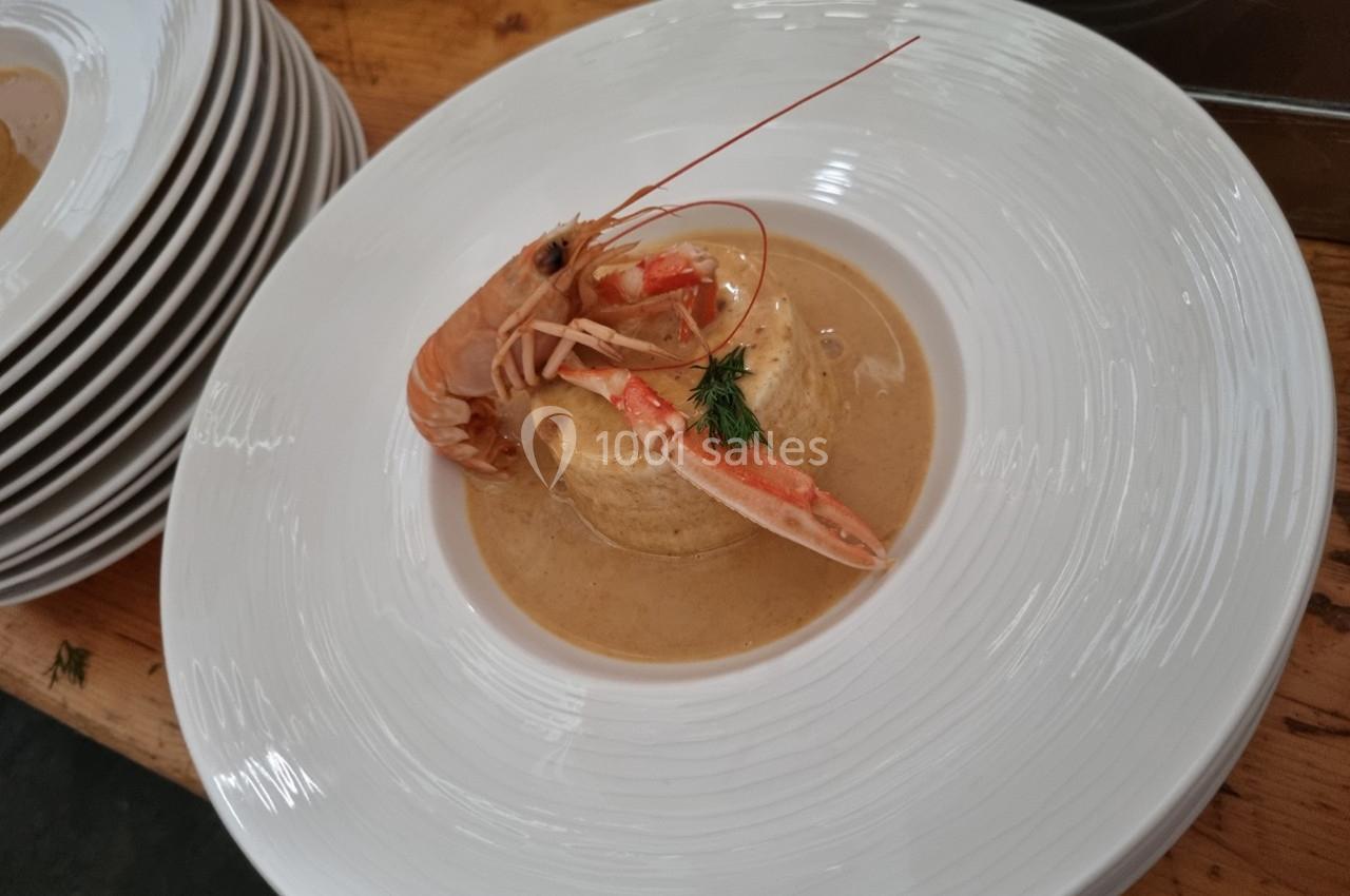 Assiette de bisque de crustacés avec une langoustine entière et une garniture d'aneth, servie sur une table en bois.