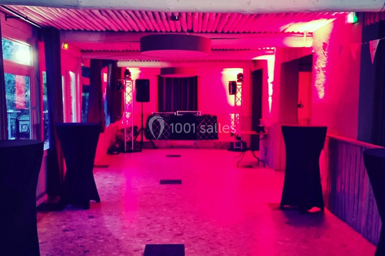 Salle de réception éclairée par des lumières rouges, avec tables hautes et équipement audio au fond.