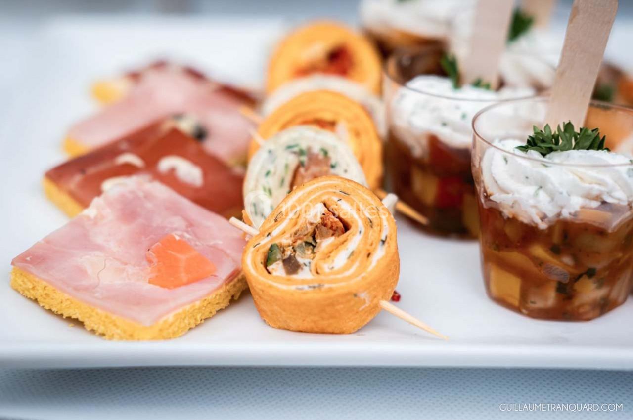 Assortiment de bouchées apéritives comprenant roulés, verrines et toasts sur un plateau blanc.