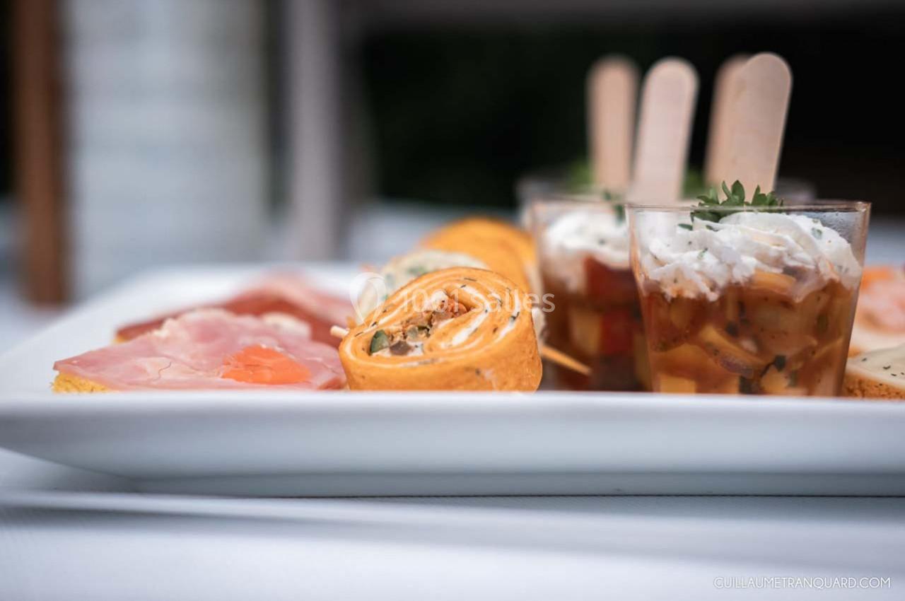Assortiment d'amuse-bouches sur une assiette, incluant roulés, charcuterie et verrines garnies.