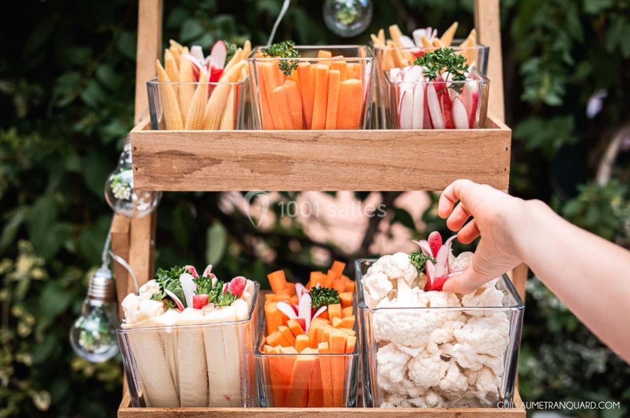 Plateau en bois avec des verrines contenant des légumes crus variés, une main prenant un radis.