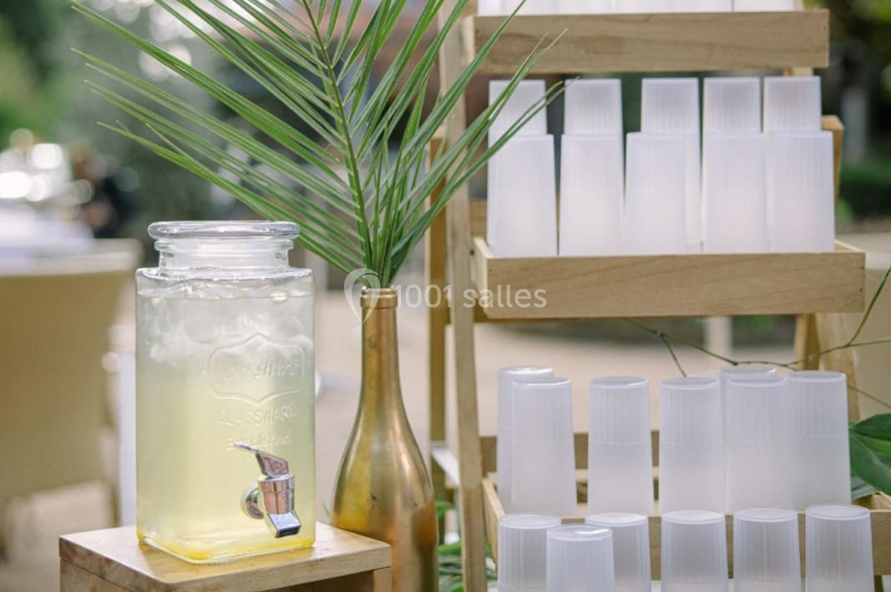 Distributeur de boisson citronnée avec des gobelets en plastique empilés sur des étagères en bois, en extérieur.