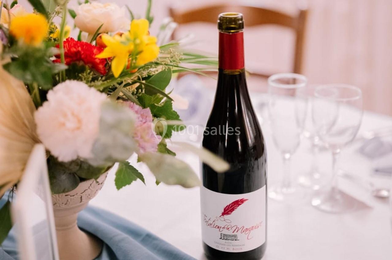 Bouteille de vin rouge posée sur une table décorée de fleurs et de verres vides.