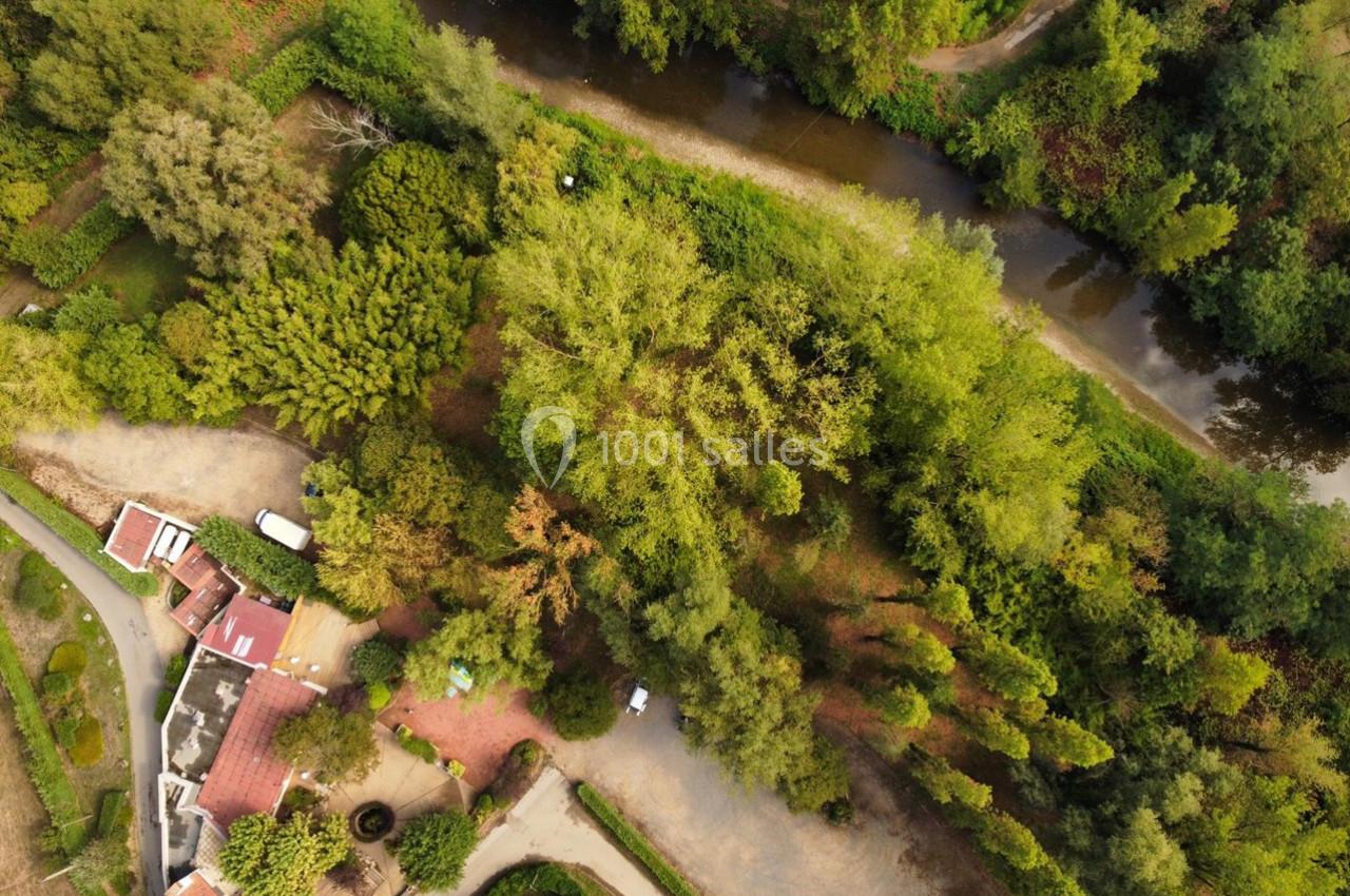 Vue aérienne d'une zone rurale avec des arbres, un cours d'eau sinueux et des bâtiments aux toits rouges.