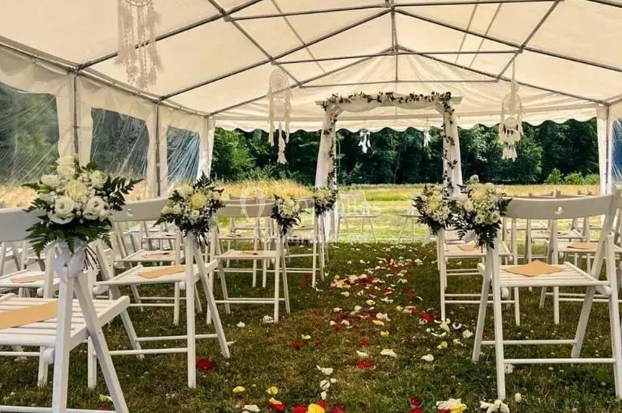 Allée décorée de pétales de fleurs menant à une arche fleurie sous une tente pour une cérémonie en extérieur.