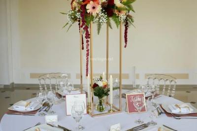 Centre de table floral avec roses roses, fleurs violettes et blanches, entouré de bougies et de verres sur une nappe blanche.