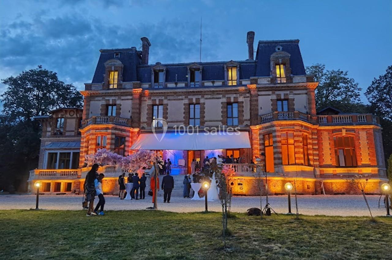 Façade illuminée d'un château au crépuscule, avec des invités rassemblés devant l'entrée principale.