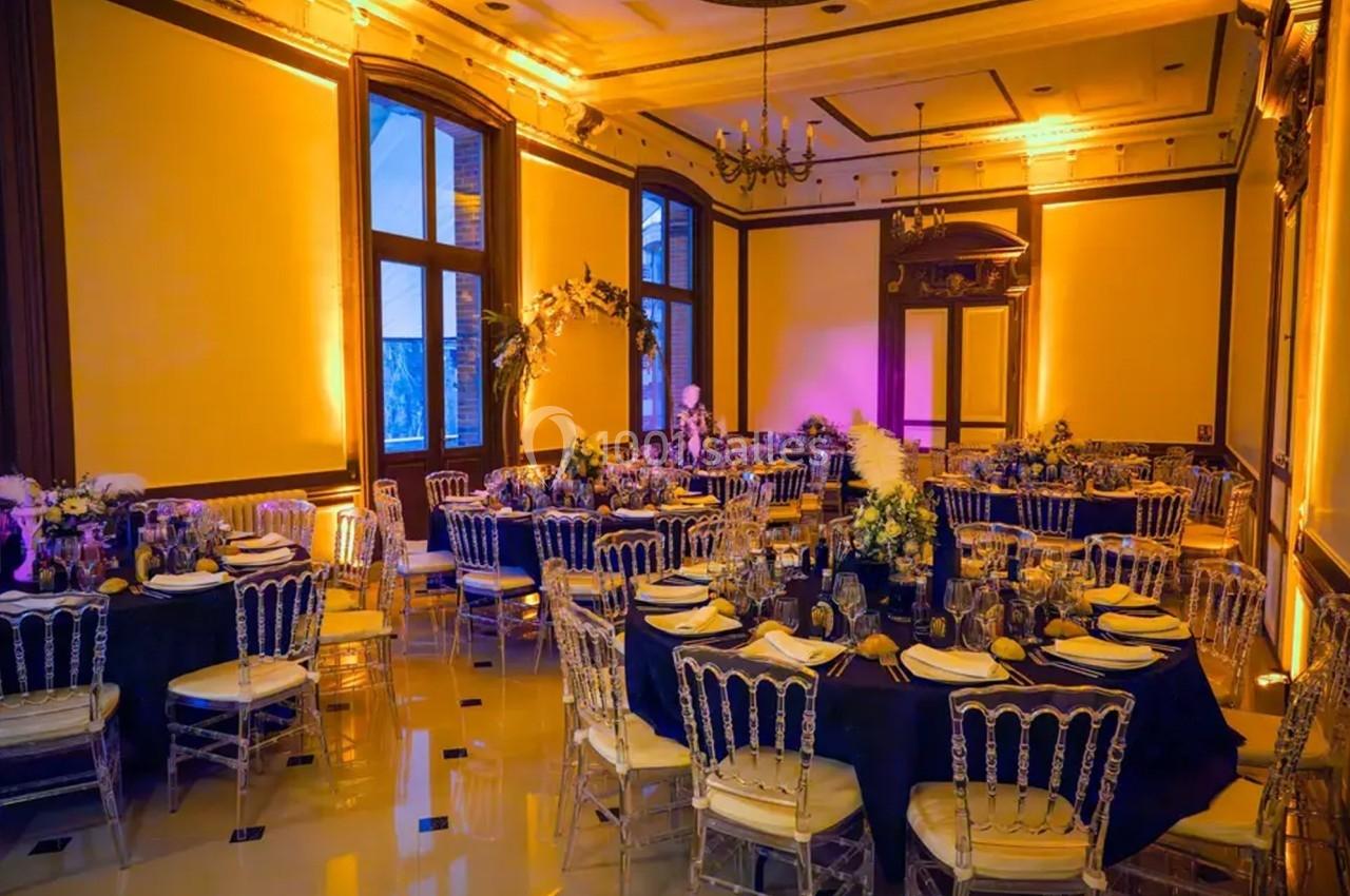 Salle de réception élégamment décorée avec des tables rondes, des chaises transparentes et un éclairage chaleureux.