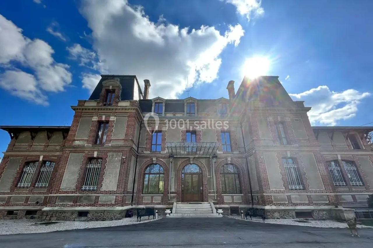 Façade d'un bâtiment en briques rouges avec toit mansardé, sous un ciel bleu partiellement nuageux.