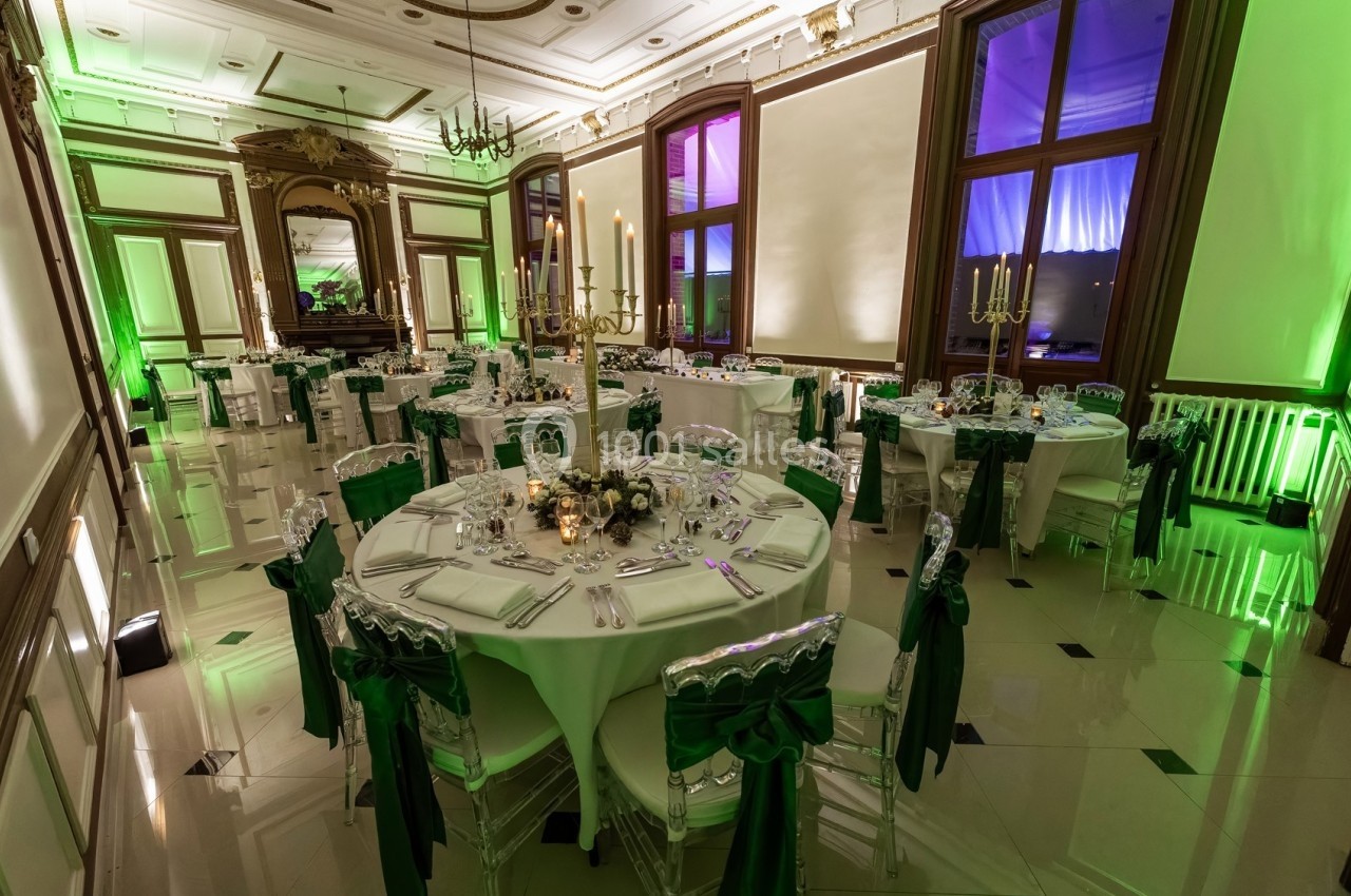 Salle de réception élégante avec tables rondes décorées de nappes blanches et chaises ornées de rubans verts.