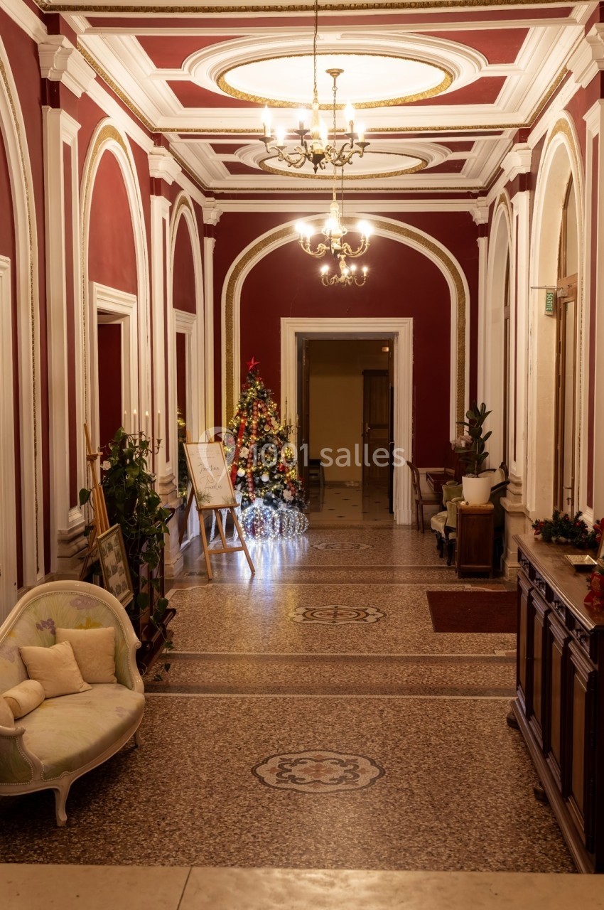 Couloir élégant avec murs rouges, sol en mosaïque, sapin de Noël décoré et meubles anciens.