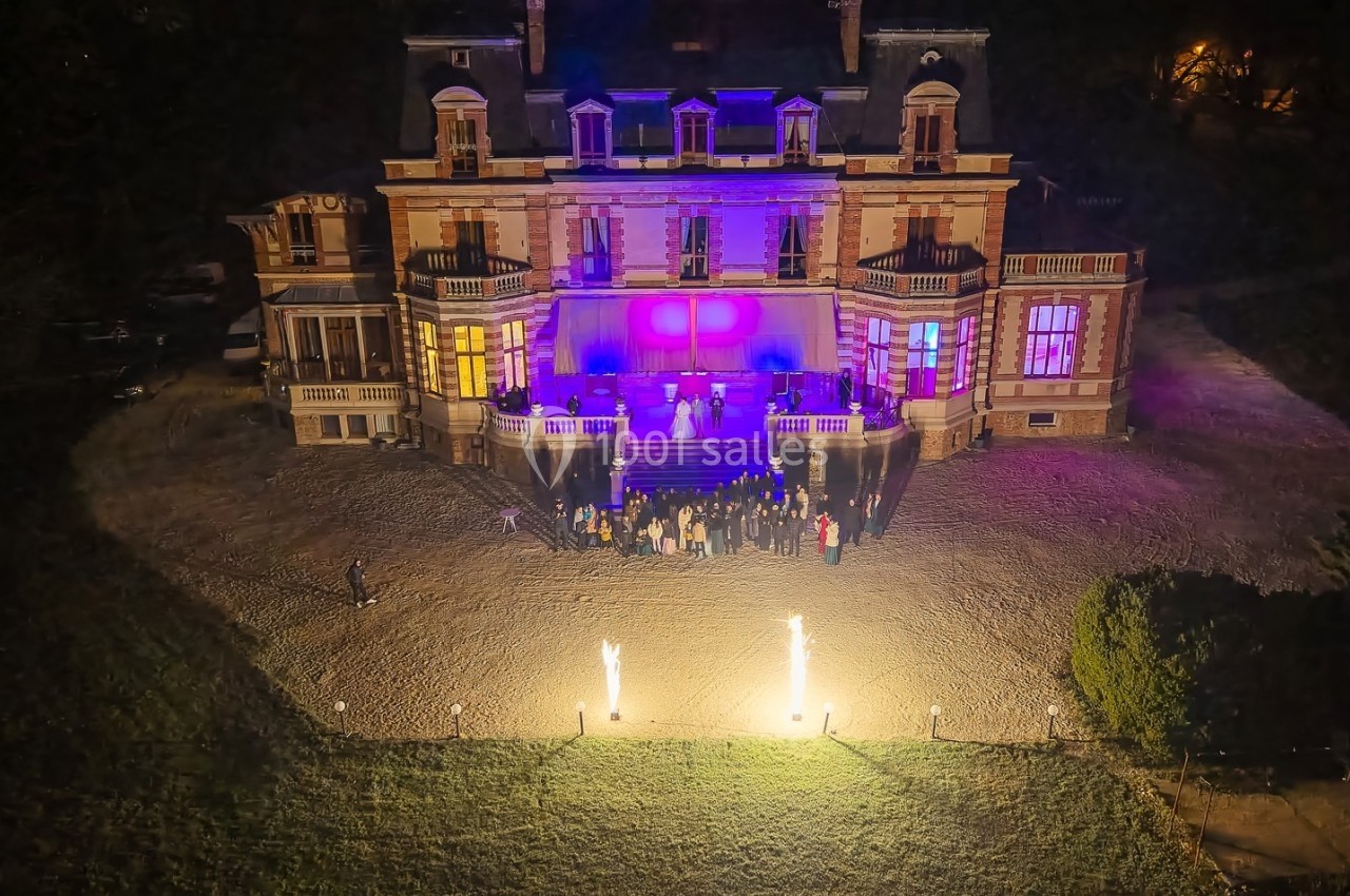 Vue nocturne d'un château éclairé par des lumières colorées, avec un groupe de personnes rassemblées devant.