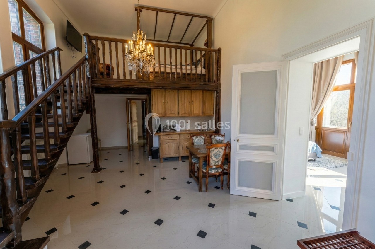 Intérieur lumineux avec mezzanine en bois, cuisine équipée en bois clair et sol en carrelage blanc.