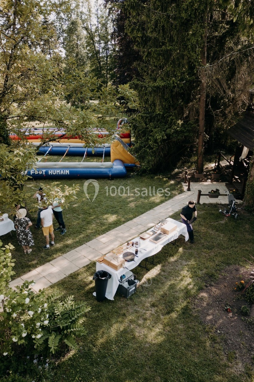 Vue aérienne d'un jardin avec des tables dressées, des personnes réunies et une structure gonflable en arrière-plan.