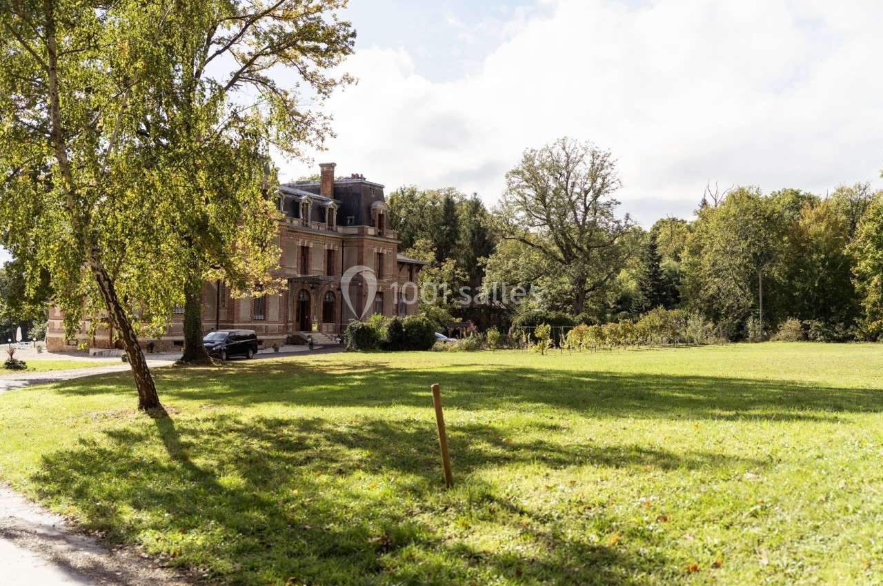 Manoir en briques rouges entouré d'arbres et d'une pelouse verdoyante sous un ciel partiellement nuageux.