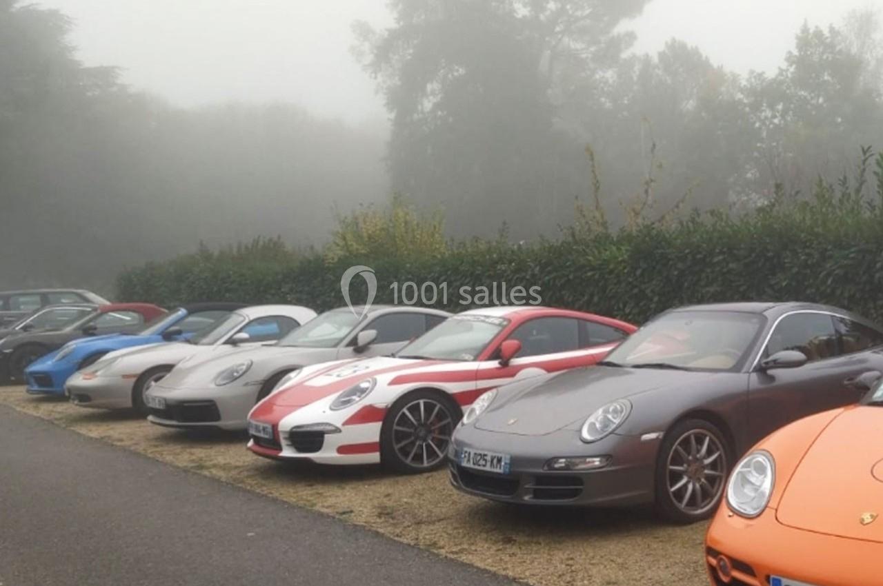 Alignement de voitures de sport colorées stationnées sur un parking en bordure de route, par temps brumeux.