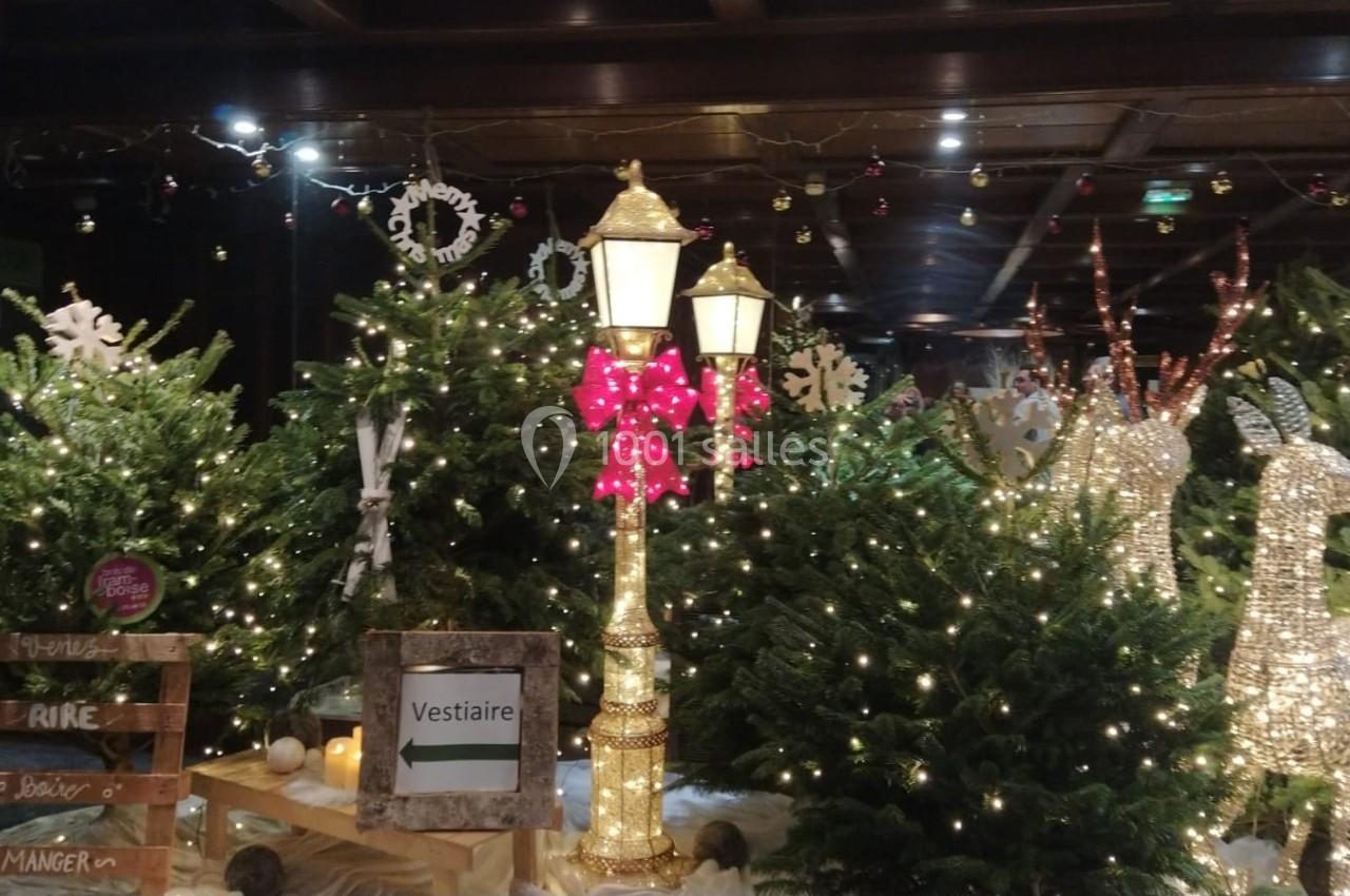 Décoration festive avec sapins illuminés, lampadaire orné d'un nœud rouge et rennes lumineux dans un espace intérieur.