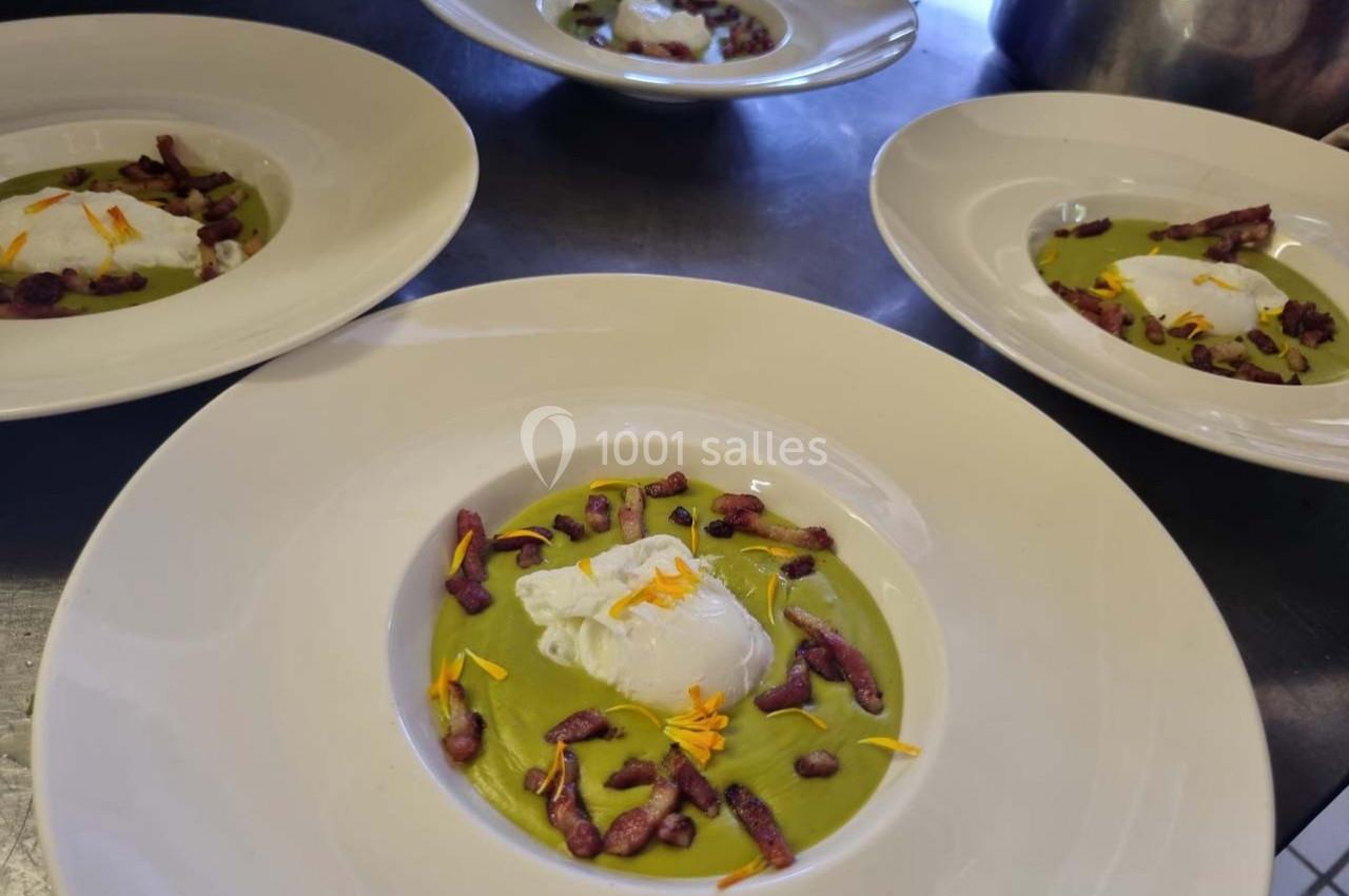 Assiette de velouté vert garnie d'un œuf poché, de croûtons violets et de pétales de fleurs jaunes.
